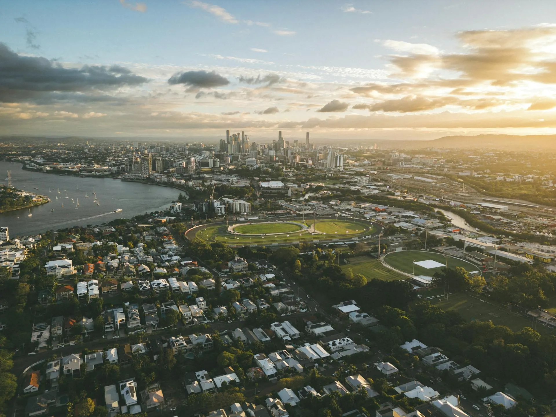 Aerial view of Brisbane at sunset, with the CBD skyline beyond the river and inner-city suburbs in the foreground